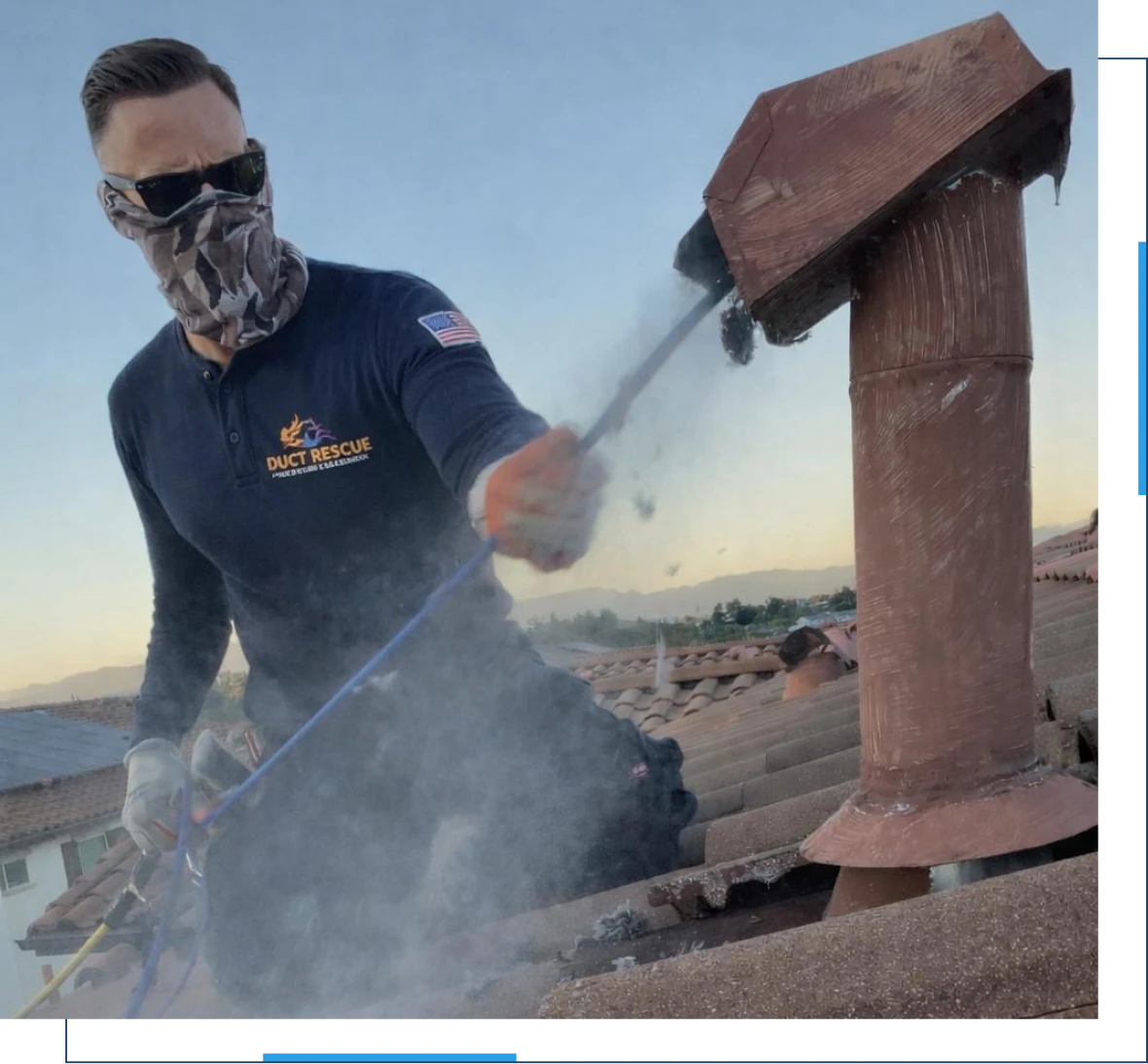 A worker wearing protective gear cleans a rooftop vent, releasing a cloud of debris or smoke into the air.